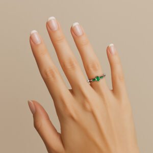 Mão vestindo o Anel de formatura Tríade em ouro 18k branco, com três esmeraldas, para os cursos de direito e jornalismo